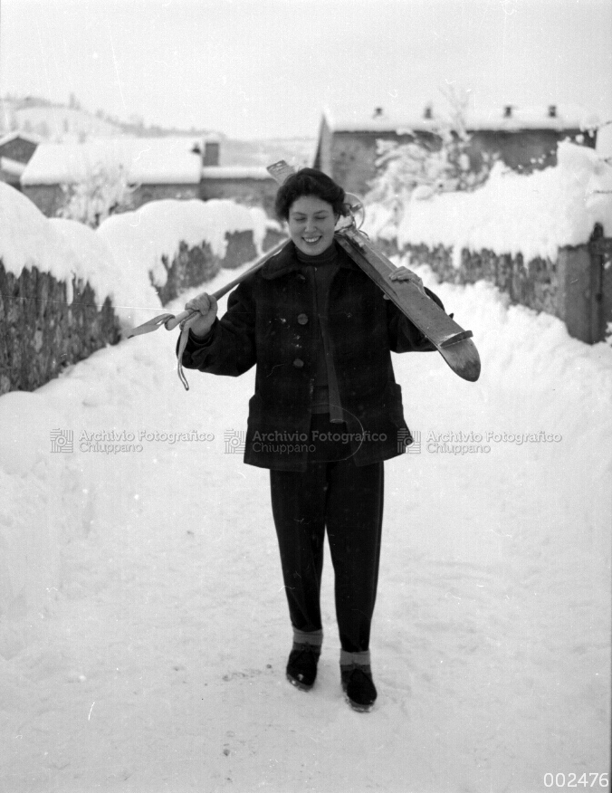 Ragazza sulla neve con scii in spalla